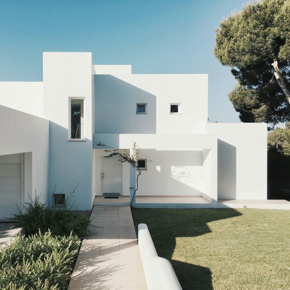 Une maison blanche aux volumes simples, sous un ciel bleu.